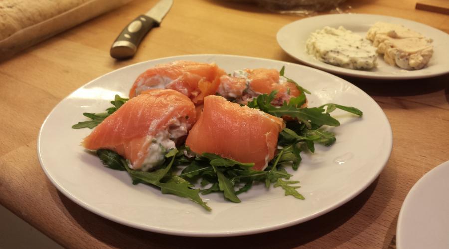 Bild zeigt: Lachsröllchen mit Frischkäse auf einem Rucola-Salatbett in der Auflösung 900x500
